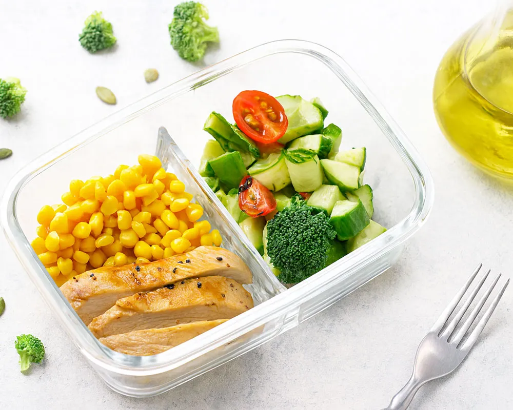 Glass meal prep containers filled with sliced chicken, grains and vegetables on a white table