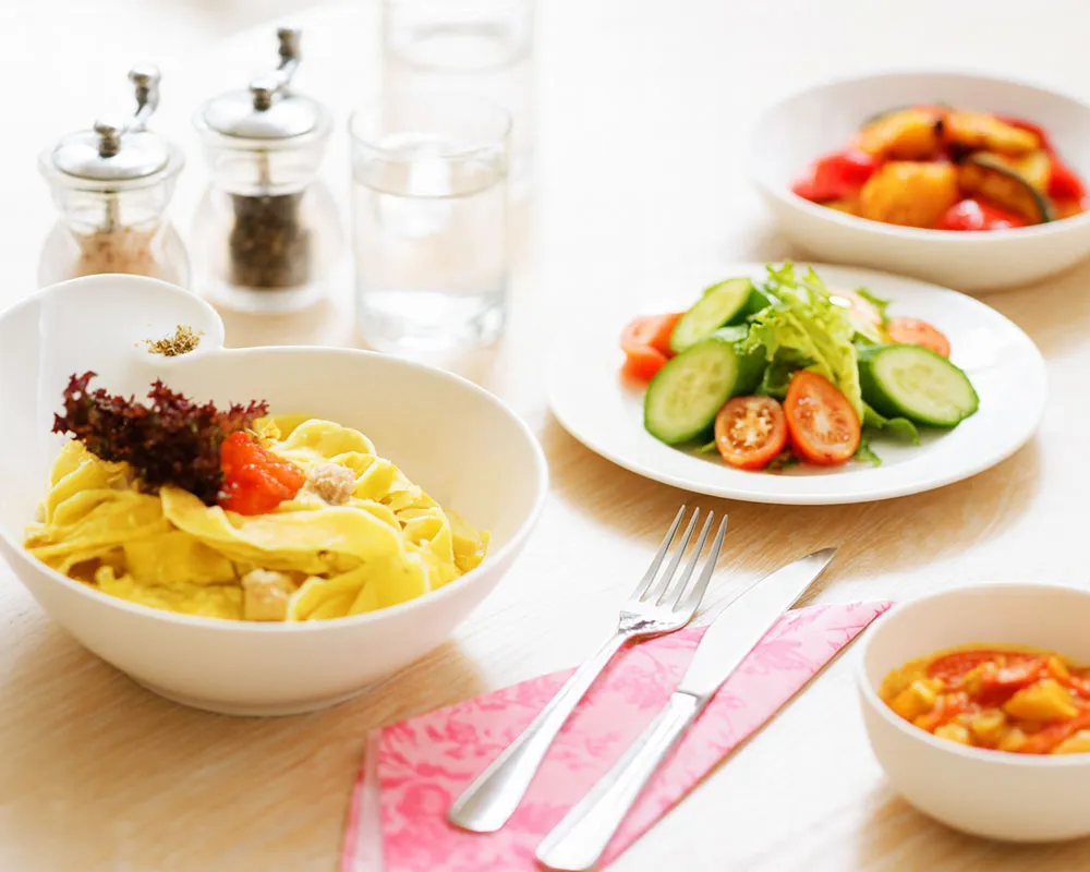 Table with bowls of creamy pasta, vegetable stew and salad showing healthy comfort food options