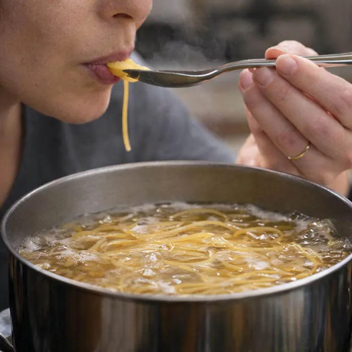 Checking Pasta Early While Cooking the cook scoops up some pasta with a spoon to check under her teeth how cooked it is
