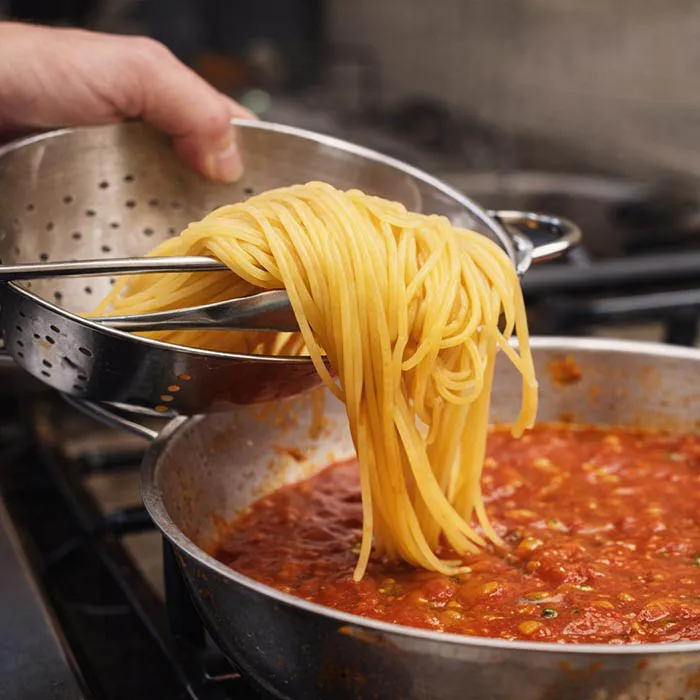 Finishing Pasta in Sauce transferring cooked pasta into sauce to finish cooking
